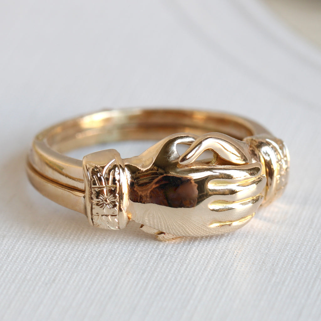 yellow gold ring that has two bands with hands that clasp and unclasp when the bands are separated or pushed togethe