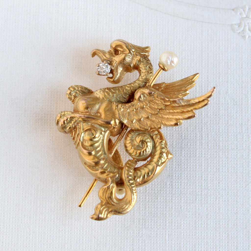 yellow gold dragon pin with a diamond in its mouth curled around a sword tipped with a pearl