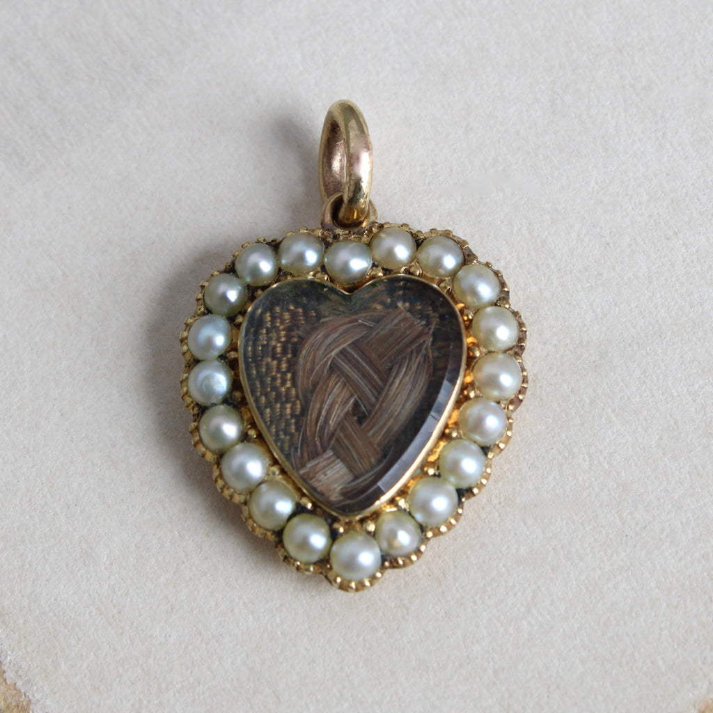 antique yellow gold heart with a woven hair love knot under glass surrounded by a frame of white pearls.
