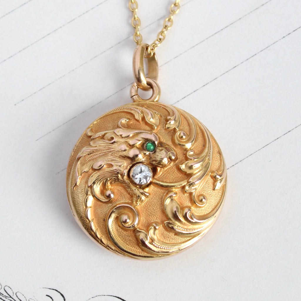 yellow gold locket with a roaring lion in a swirl of scroll designs holding a bright diamond in his mouth