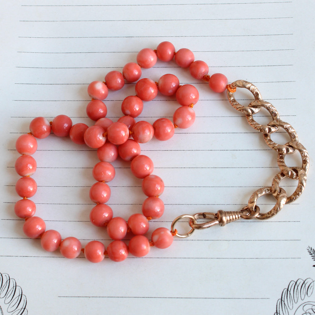 round salmon colored natural coral beads with a section of antique decorative curb chain and a dog clip clasp