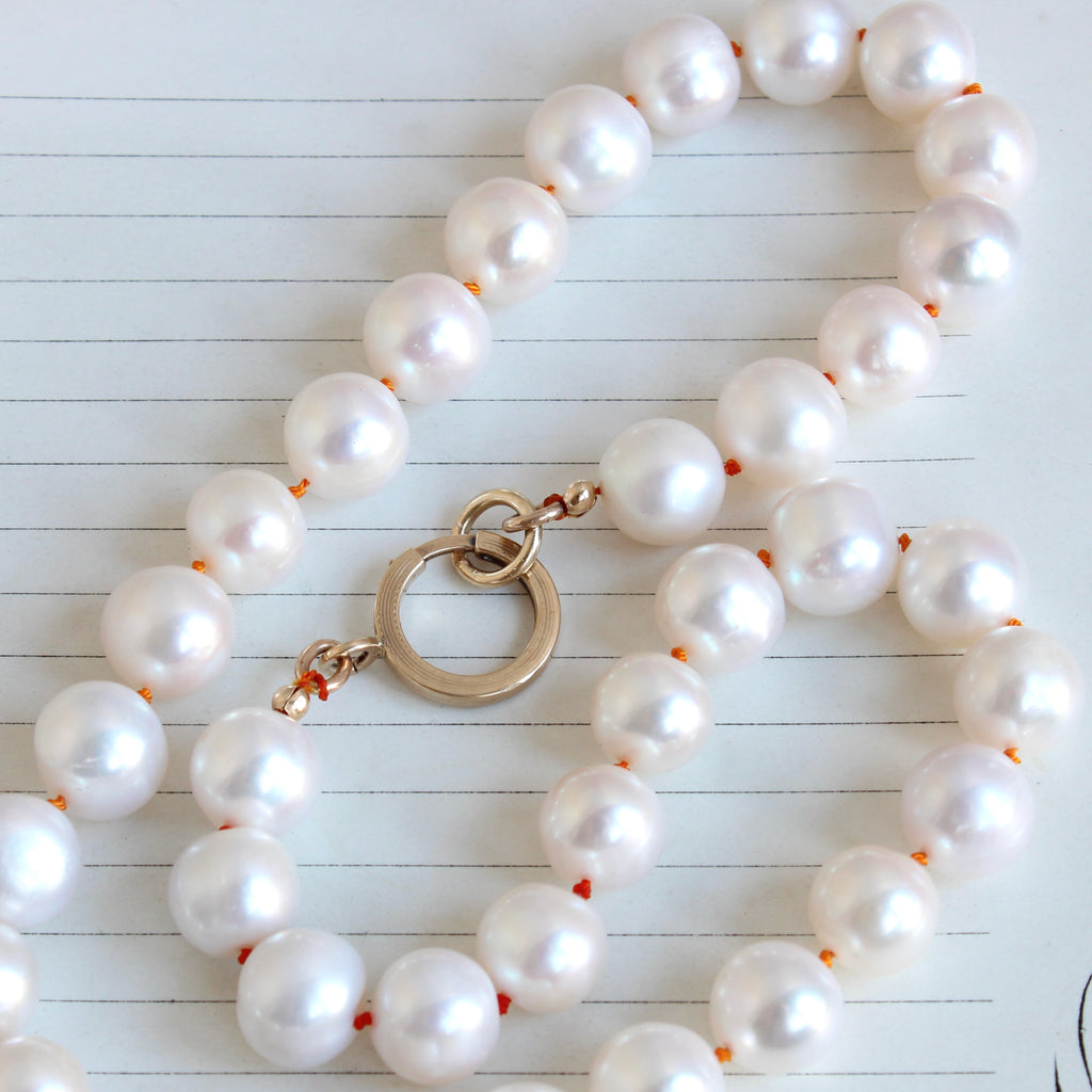 large cultured pearls knotted on orange silk with a large gold bolt ring charm holder clasp