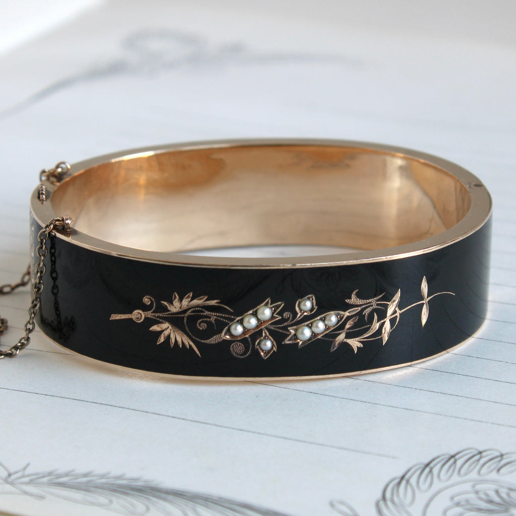 yellow gold bangle with lily of the valley motif set with seed pearls on a balck enamel backround