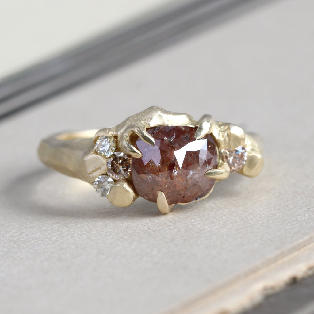 organic style yellow gold ring set with a cushion shaped cinnamon colored rose cut diamond in the center and earth tone colored full-cut diamond accents