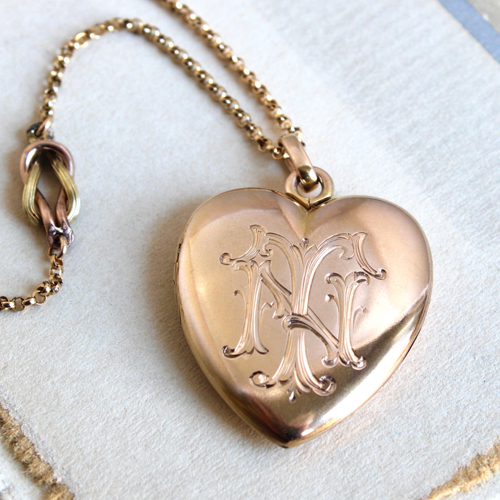 rosy yellow gold heart locket engraved with initials N.T. on a chain with a love knot charm accent