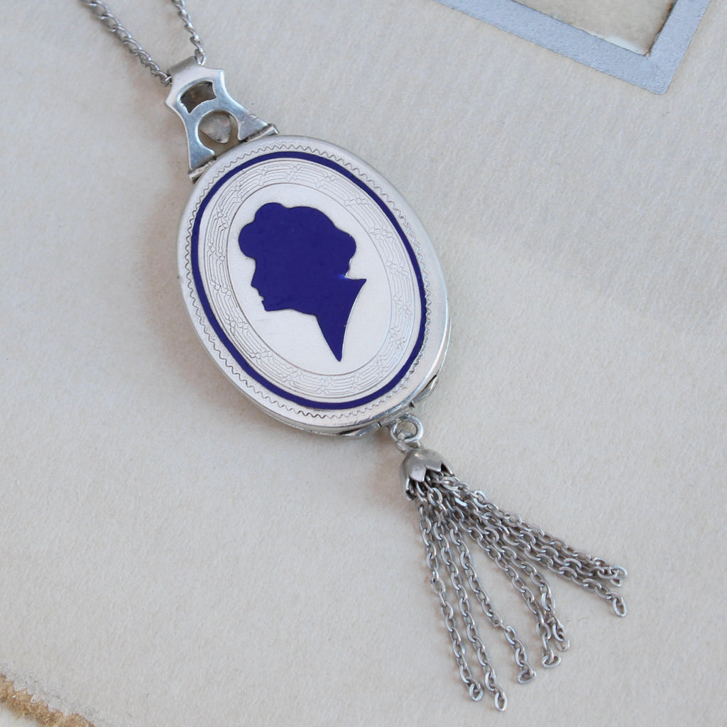 antique silver oval locket with a profile portrait of a woman with upswept hair done in cobalt blue enamel, a silver tassel hangs from the bottom