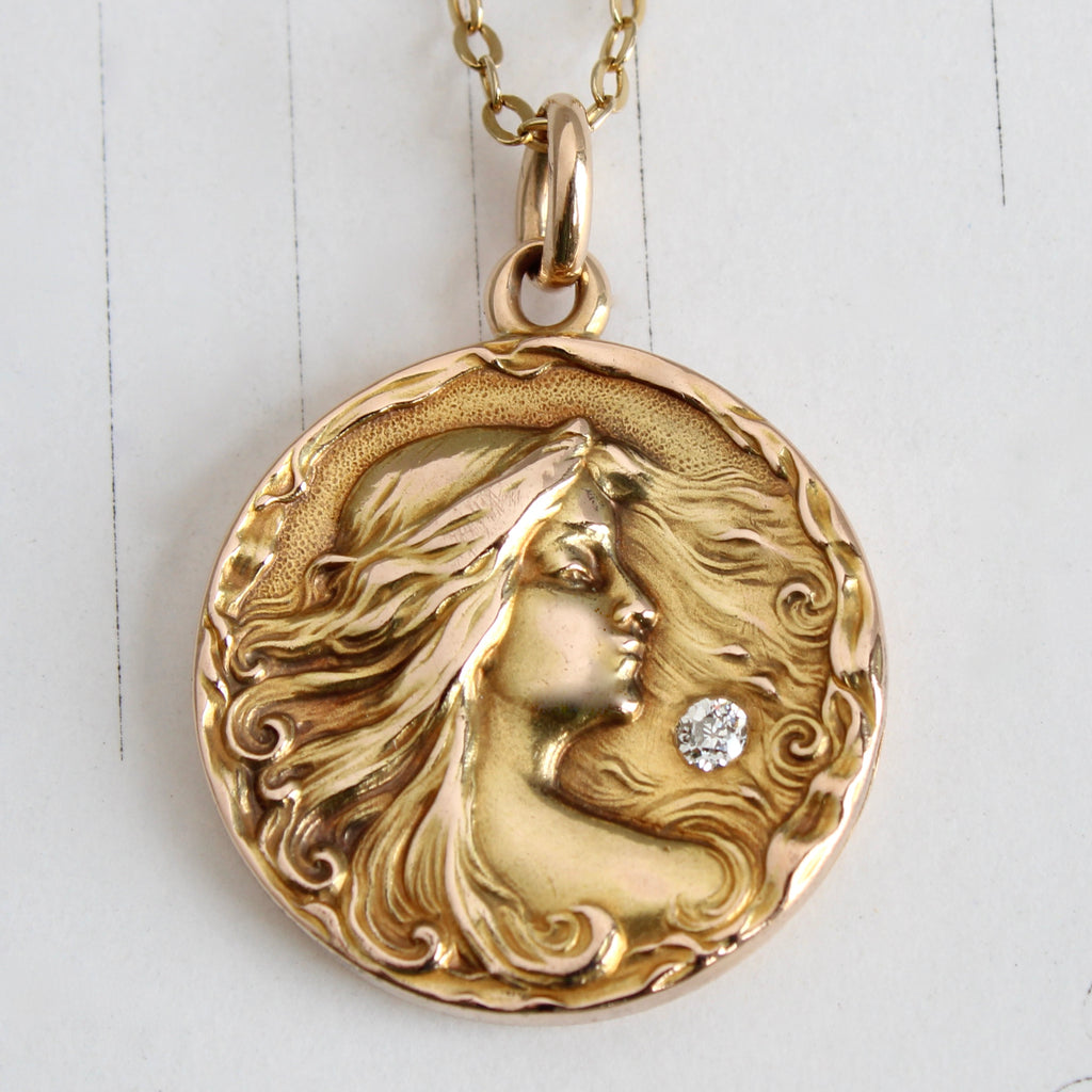 gold locket with profile portrait of lady with windswept hair accented by a bright old cut diamond