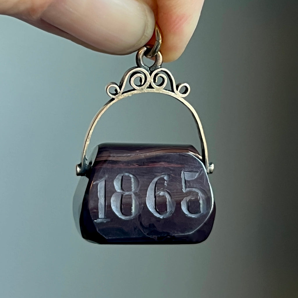 Victorian fob with a brown agate stone carved with the date 1865 hanging from a solid gold bail.