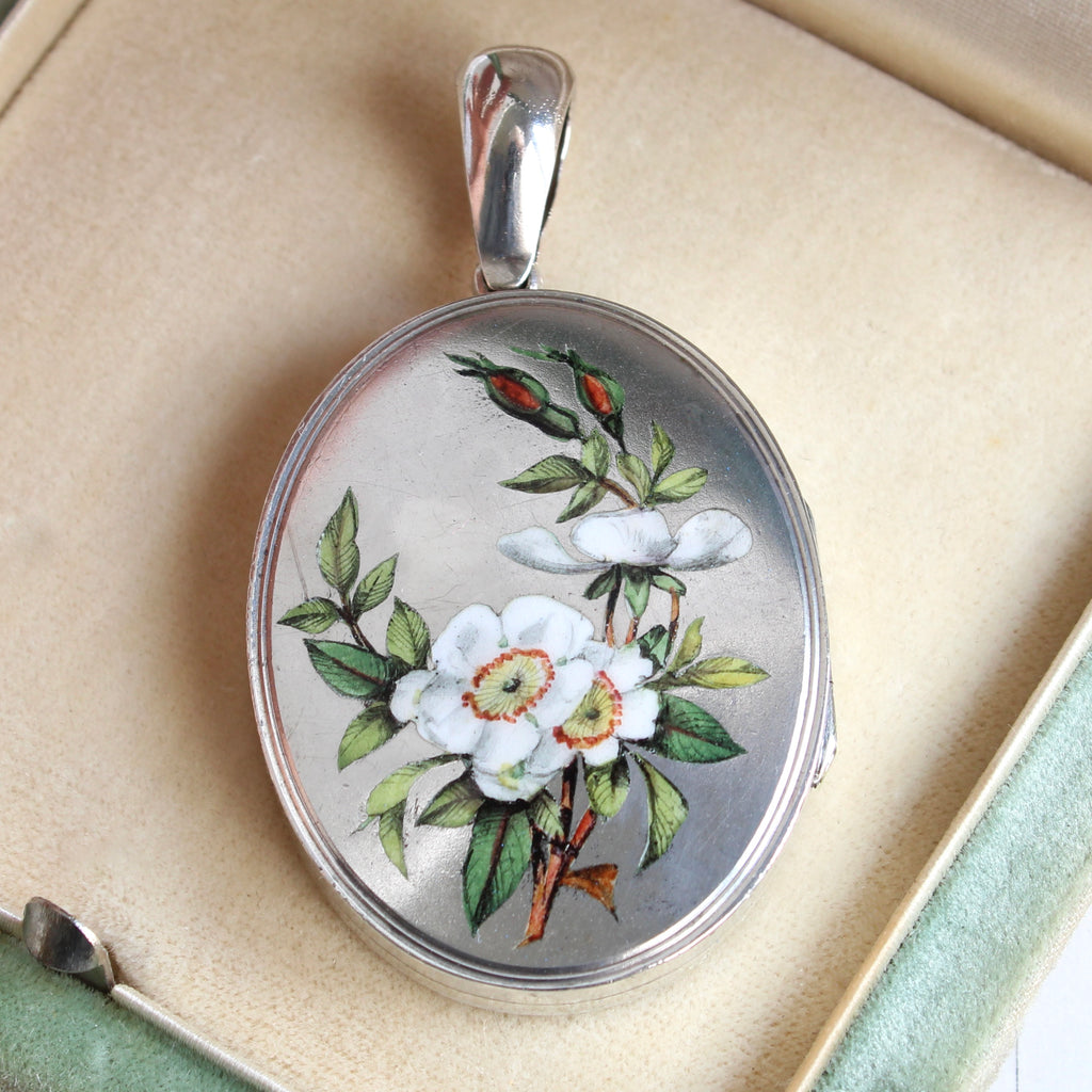 antique silver locket with a spray of realistic wild white roses enameled on the front and an engraved meadow scene on the back