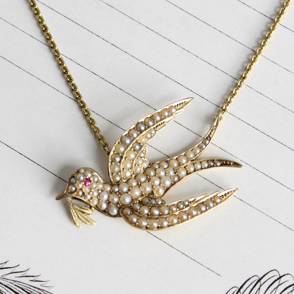 Antique yellow gold flying dove pendant set with tiny white pearls and a ruby eye on gold chain
