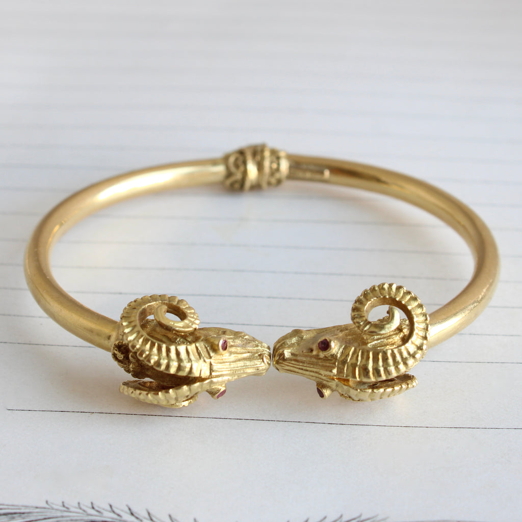 yellow gold bangle bracelet designed as a pair of kissing rams with curled horns and ruby eyes