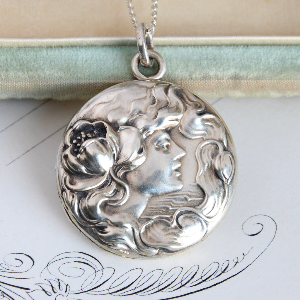 silver locket embossed with the profile of a woman with windswept hair and a water lily