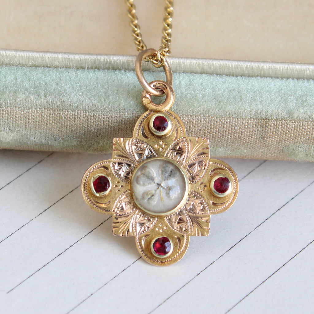 gold charm with a four leaf clover painted under glass and four red accent gems, on a gold chain