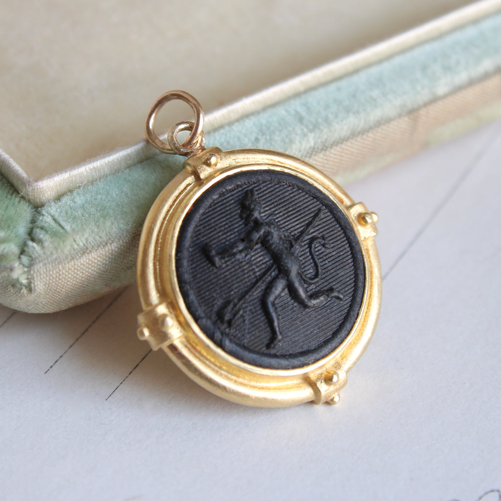 black glass cabochon molded with image of a running devil in a yellow gold pendant mounting 