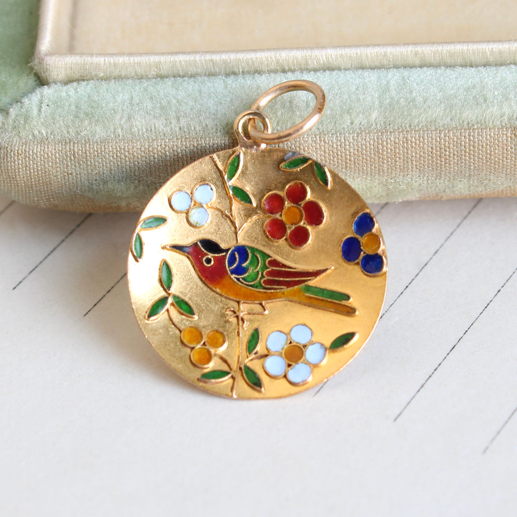 round gold charm with multi color enamel scene of a bird and flowers