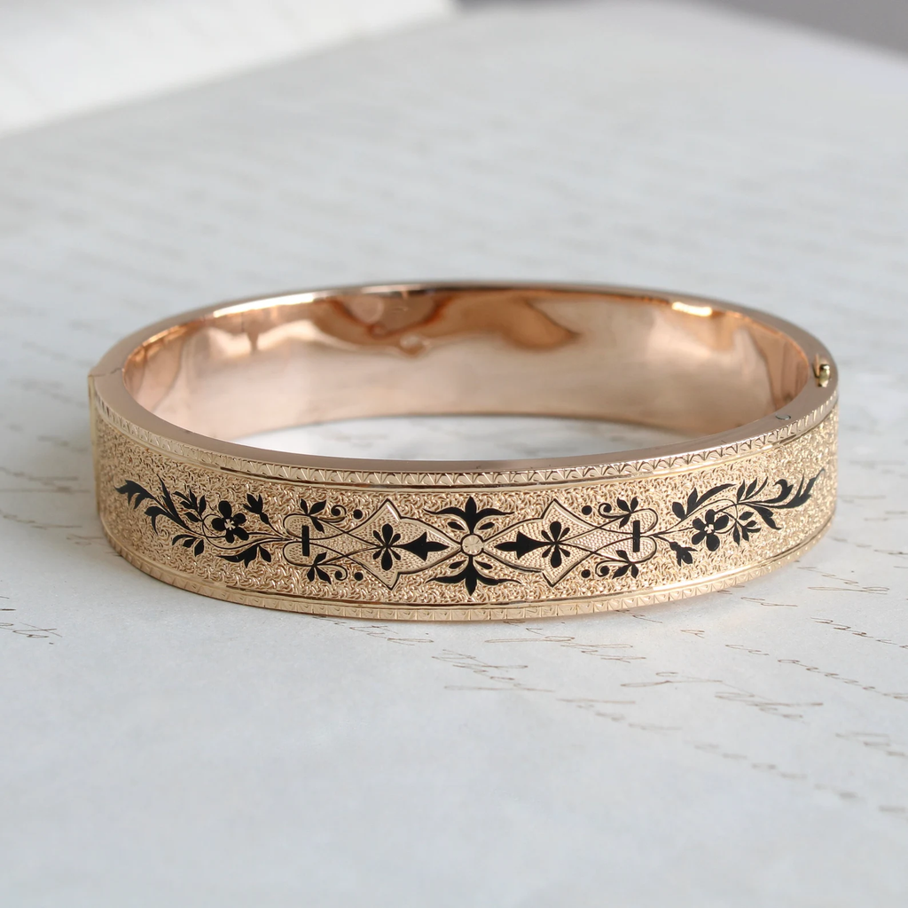 Antique yellow gold bangle bracelet with stippled surface texture and black enamel forget me not flower motif all around outside .