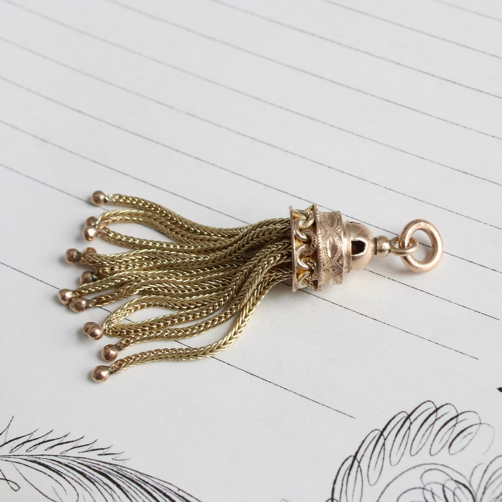 Antique yellow gold tassel charm with braided gold string and a domed top.