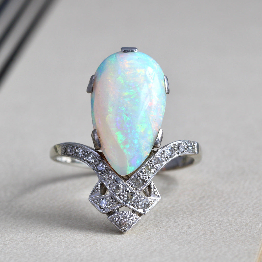 Antique white gold ring with a colorful teardrop shaped opal on a diamond studded bow motif band
