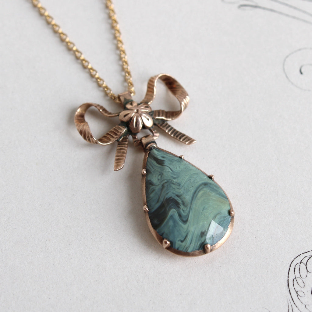 Antique yellow gold pendant necklace with a green paste teardrop topped by a bow and a tiny blossom at the knot.