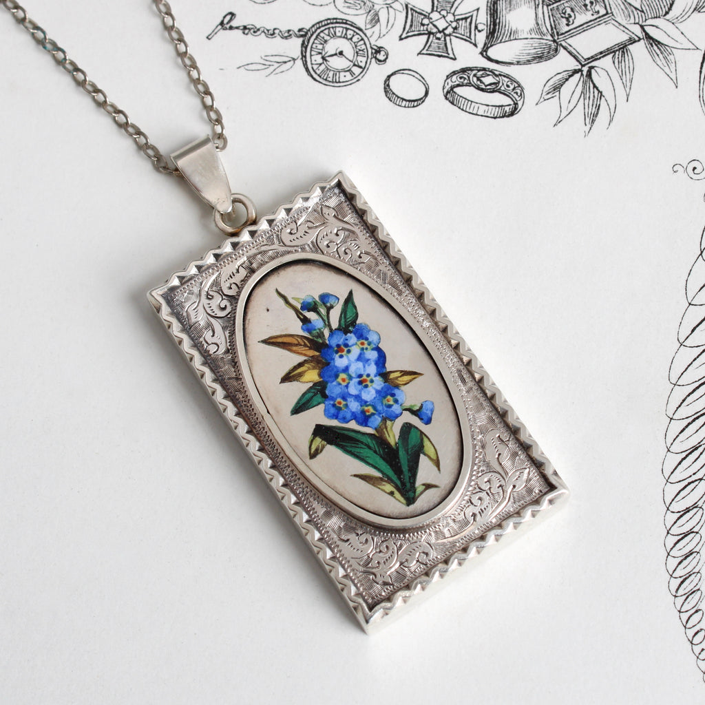 Antique sterling silver rectangular locket with an enamel painting of blue Forget Me Not flowers.