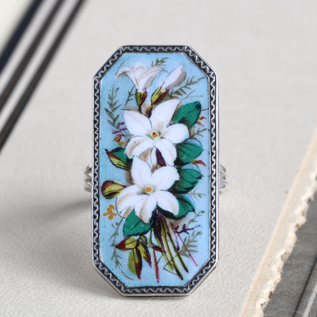 Antique sterling silver ring with a large enameled painting of orange blossom flowers with a baby blue background.