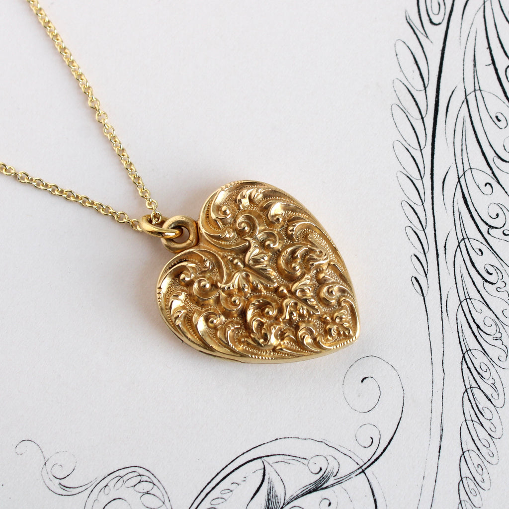 Antique yellow gold heart lockets with embossed filigree designs hanging on a yellow gold cable link chain.