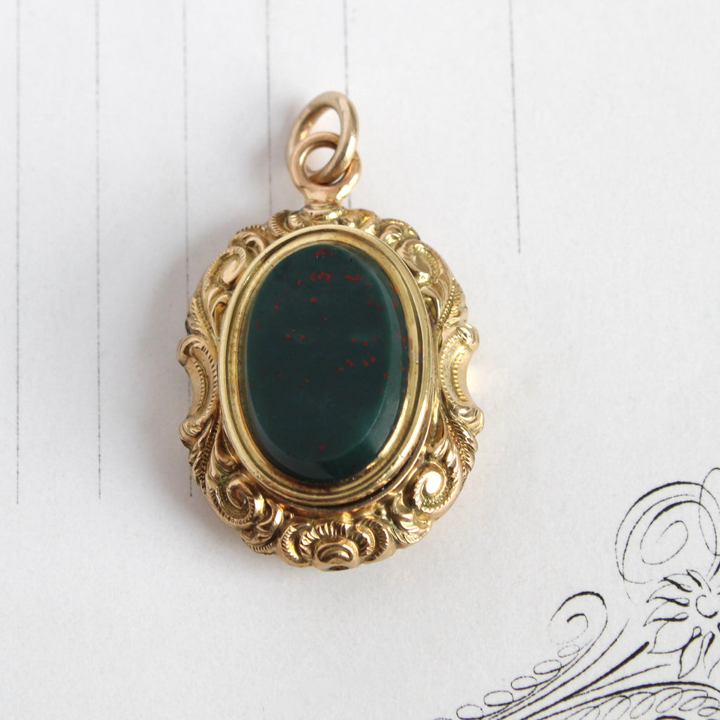 Antique yellow gold oval locket with a bloodstone center stone and scroll design border.