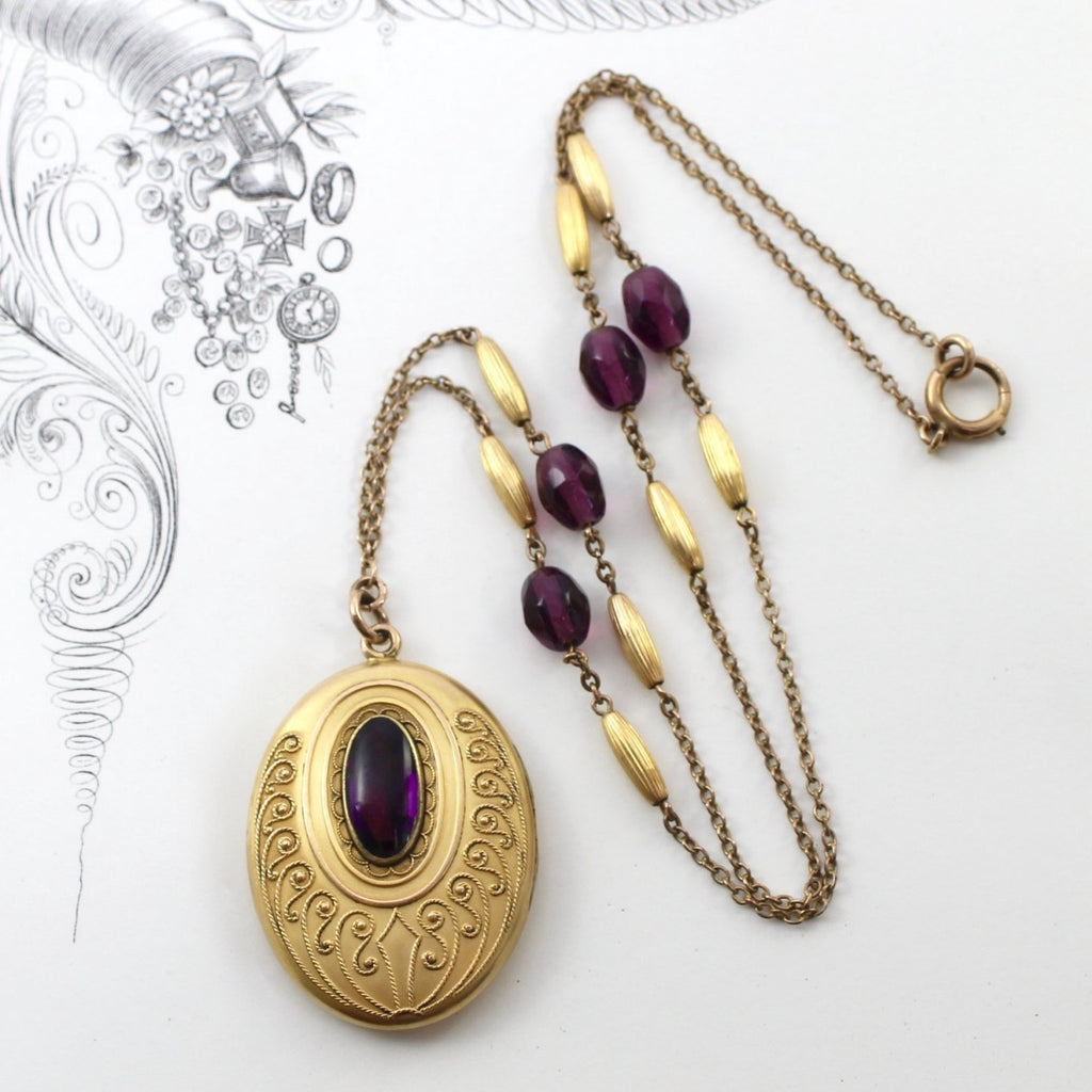 Antique yellow gold oval locket with a amethyst paste cabochon in a bezel setting and filigree designs, hangs on a beaded cable link chain.