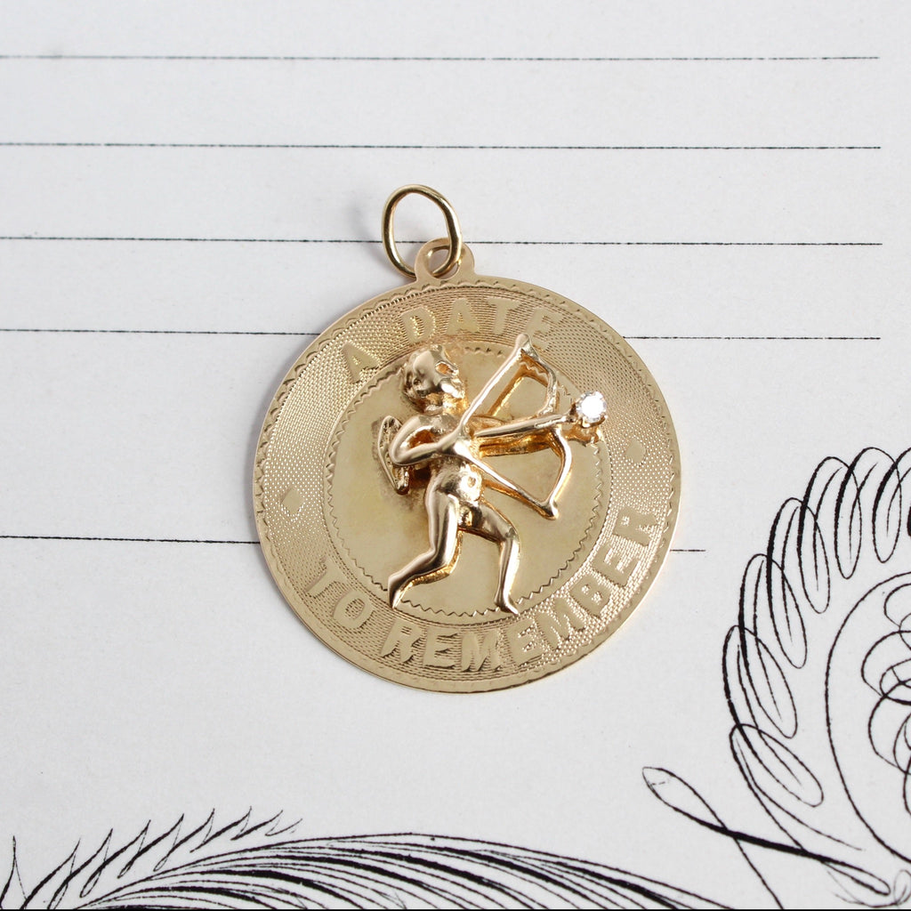 vintage yellow gold coin charm with a cupid holding a bow and engravings.