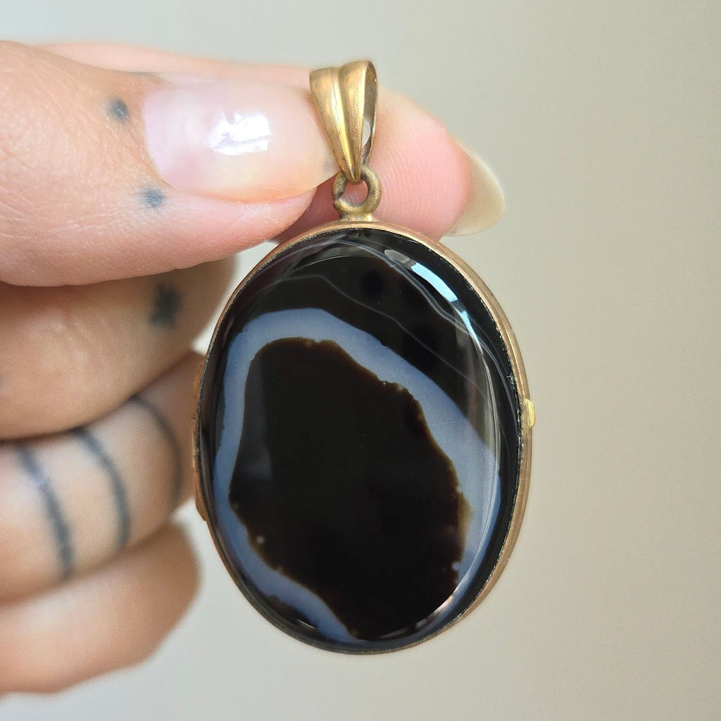 locket with polished black and white agate covers in a yellow base metal frame.