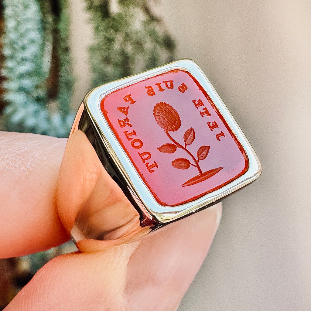 side view yellow gold ring with inlaid face of orange stone carved with french words and a flower