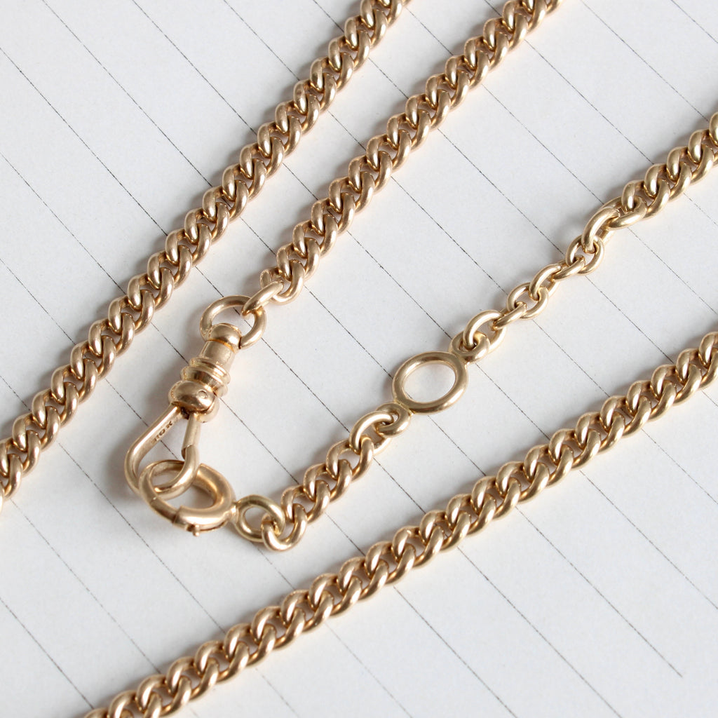 yellow gold rounded curb chain necklace with a charm holding clip clasp on one end and spring ring bolt clasp on the other