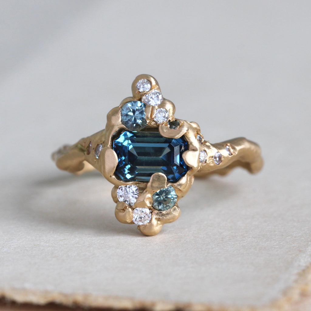 branch style gold ring set with a radiant cut teal blue sapphire and diamond and pale blue spinel accents