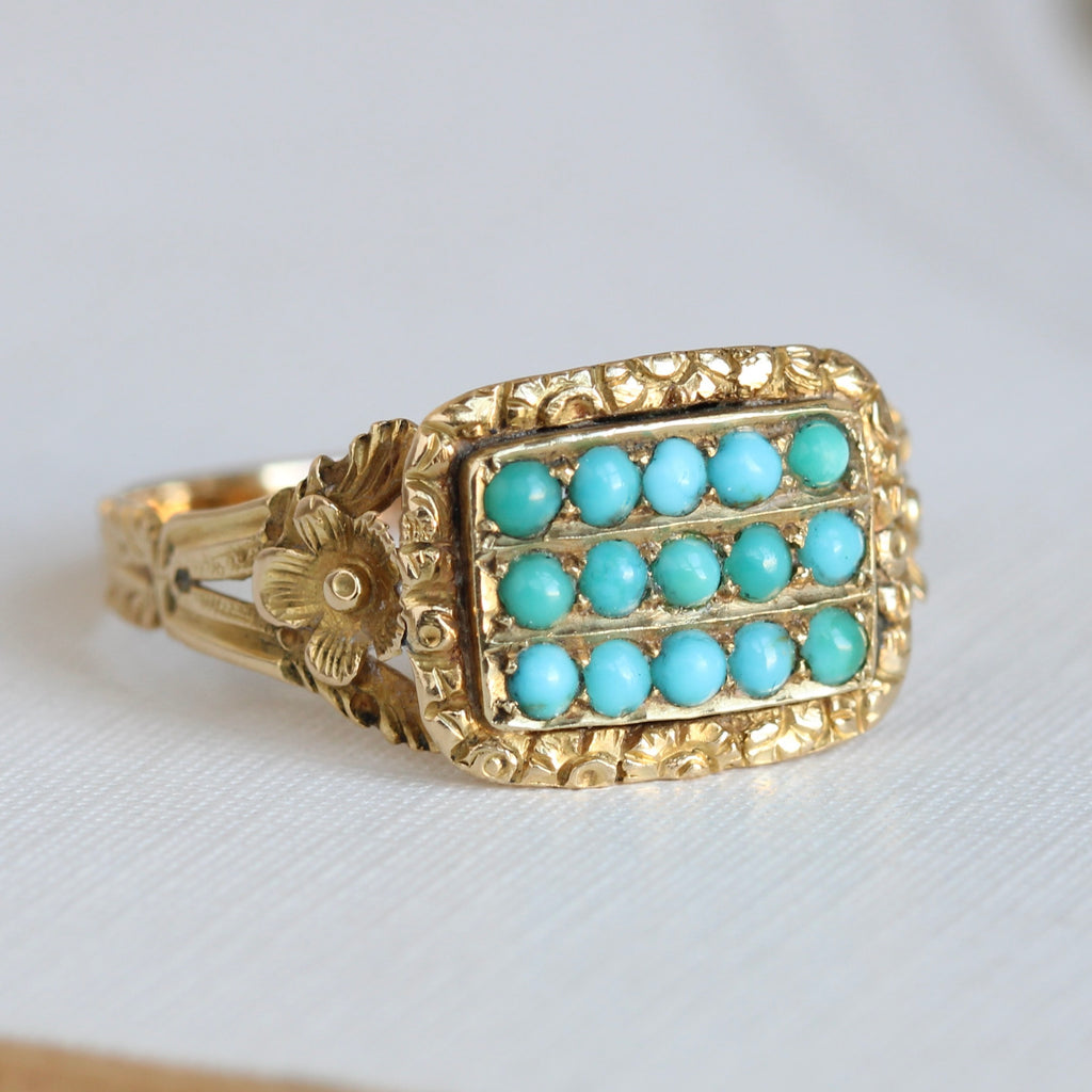 high karat yellow gold ring with three rows od small turquoise cabochons across the front and a chased floral design around the face. Each shoulder has a small flower at the top.