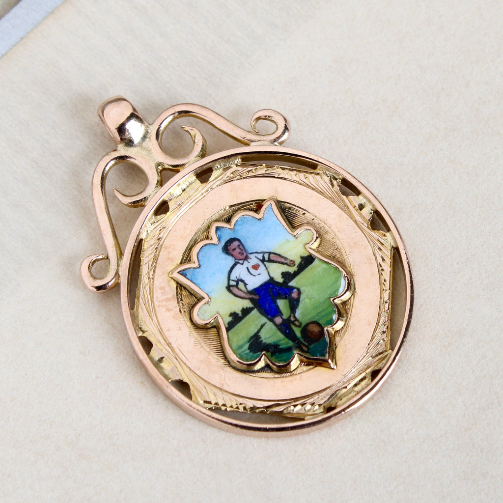 rose gold medal with a scrolled top and enameled  scene of a football or soccer player about to kick a ball