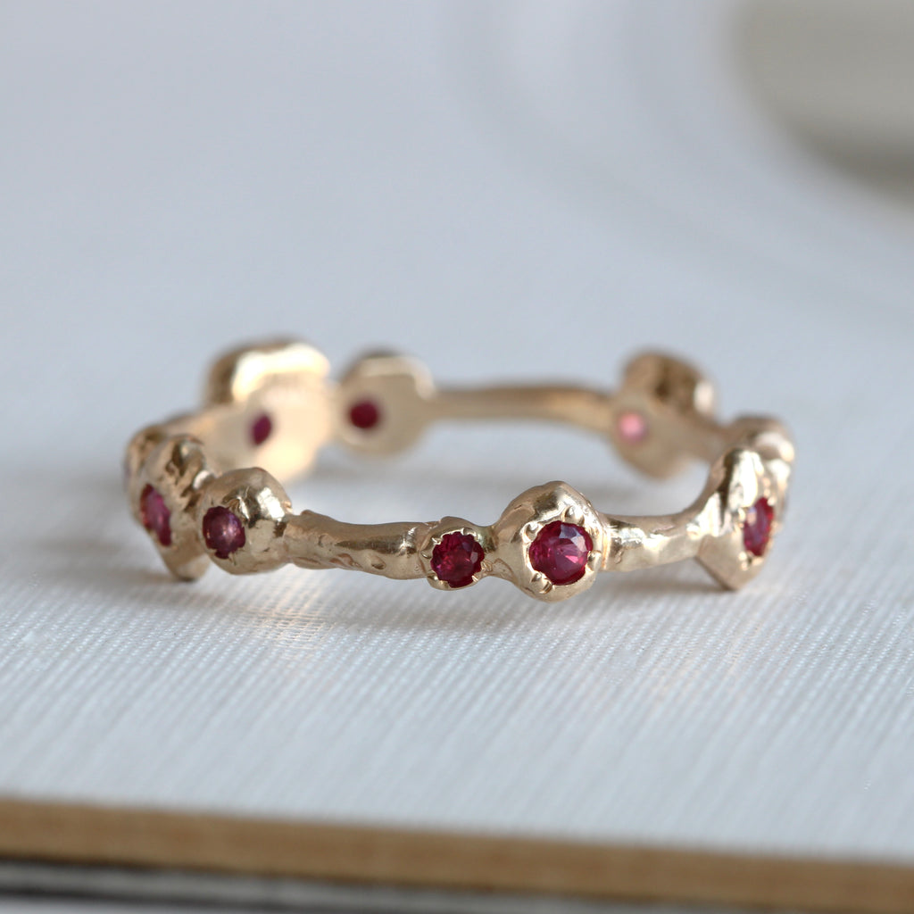 eternity band in yellow gold designed as organically shaped stations each set with a different red or pink gemstone