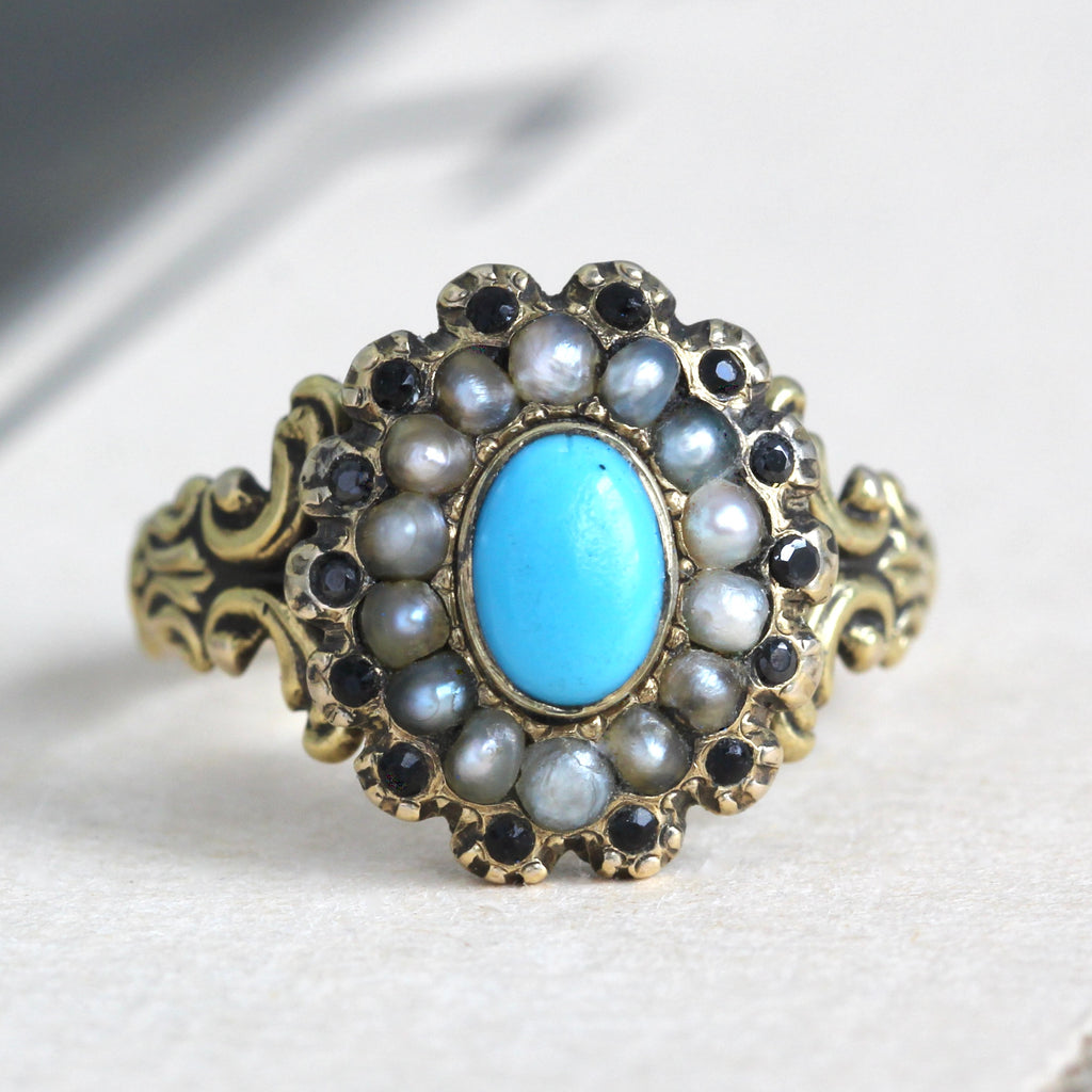 yellow gold ring with an oval turquoise paste gem surrounded by a halo of white pearls and a second halo of faceted jet.