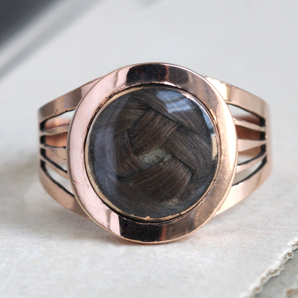 Antique rose gold ring with a glass dome in the center covering a love-knot woven of brown hair.