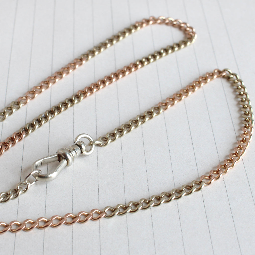 curb chain necklace of alternating rose gold and white gold sections with a white gold charm clip clasp