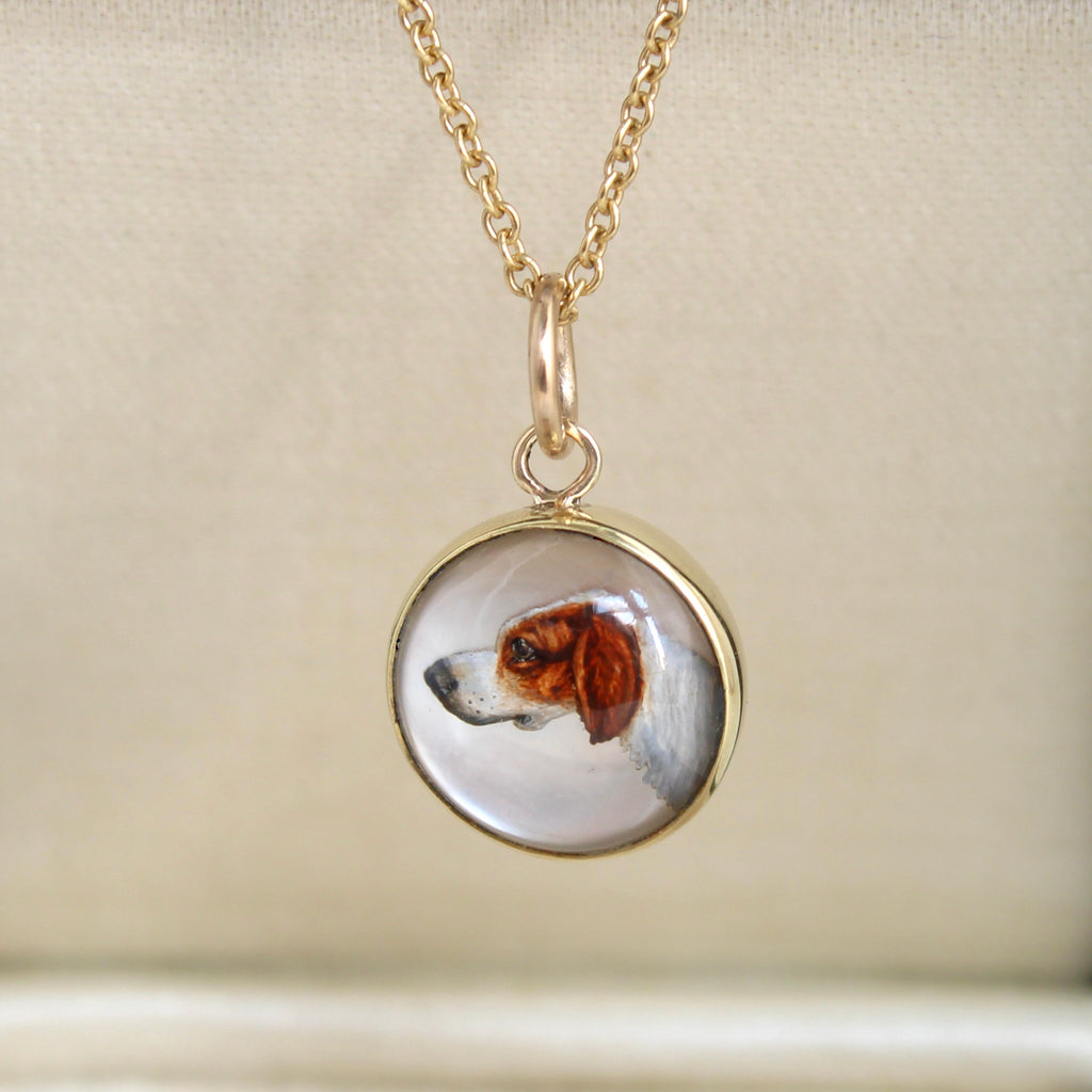 a portrait painting of a beagle on mother of pearl under a glass dome set as a gold charm with a gold chain