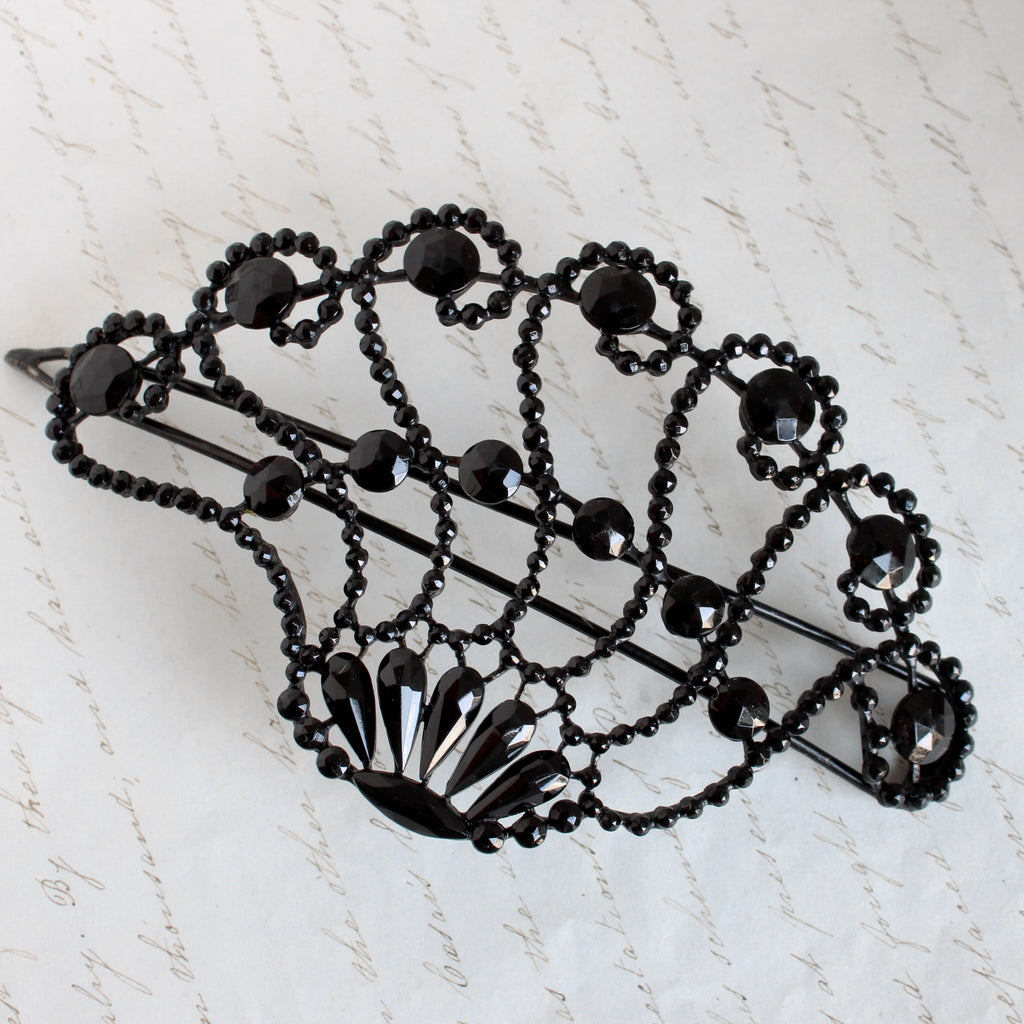 a large antique barrette with small black glass jewels arranged in a lacey scallop design on an openwork wire frame