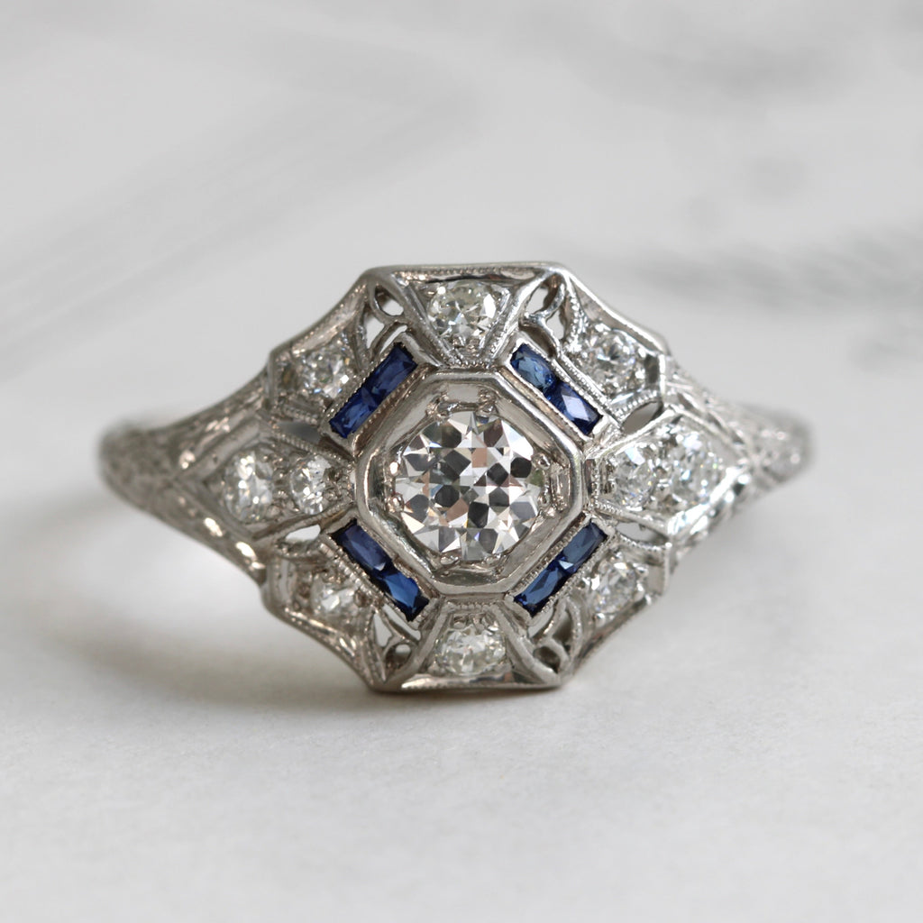 silver metal platinum ring with old cut diamonds and a lacy filigree design with sapphire baguette accents