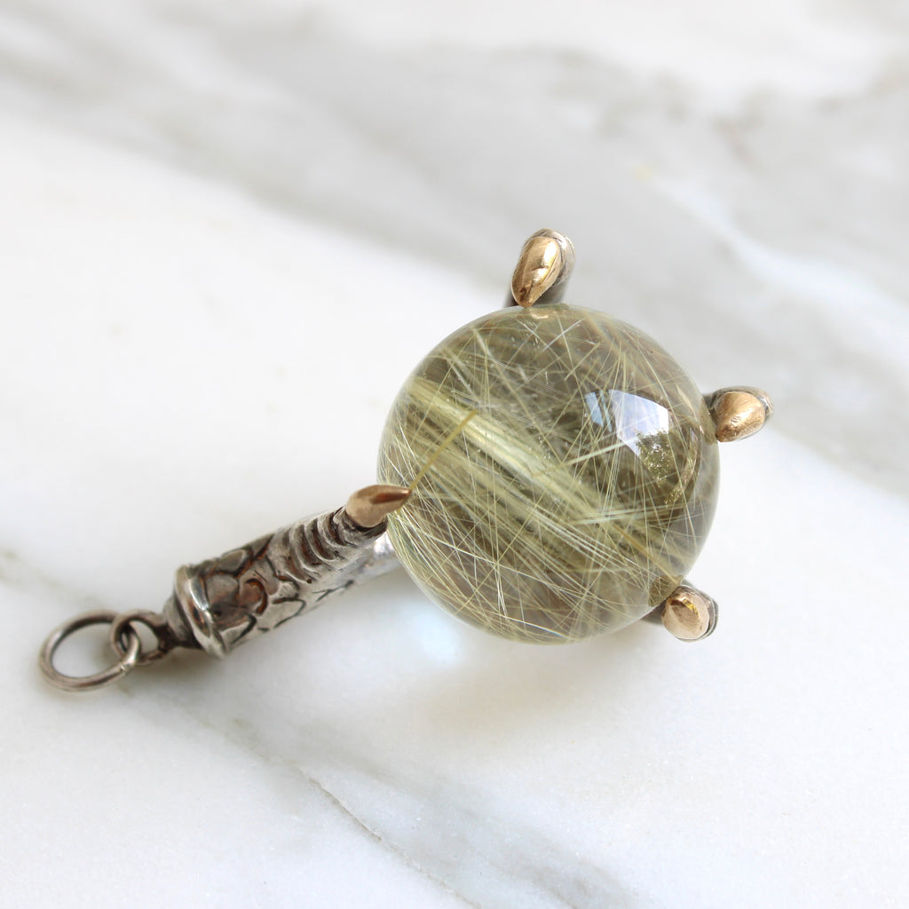 carved silver bird claw pendant holding rock crystal ball that has golden needle formations inside