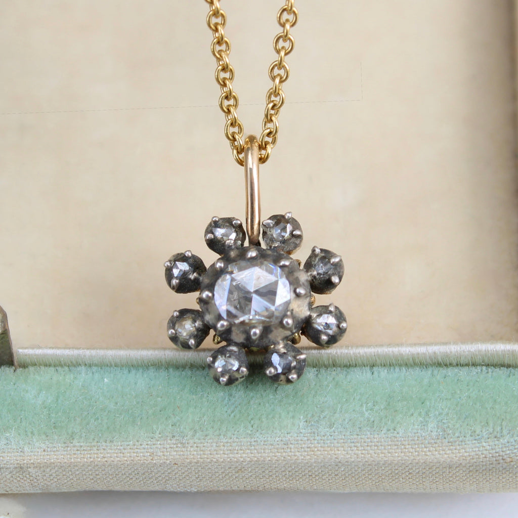 pendant of antique oval rose cut diamond with a cluster frame of smaller round rose cut diamonds set in silver on a gold chain
