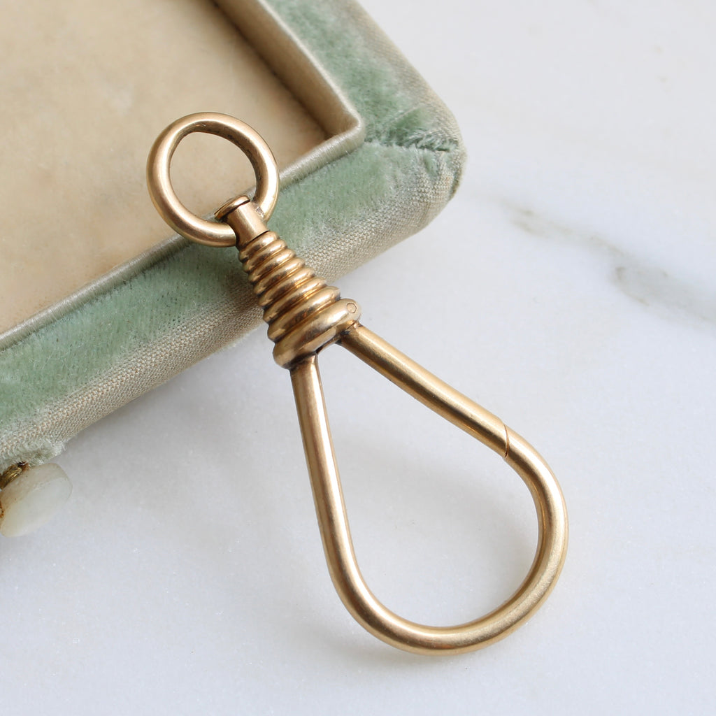 a large gold tear drop shaped clasp that opens on one side called a dog or watch clip