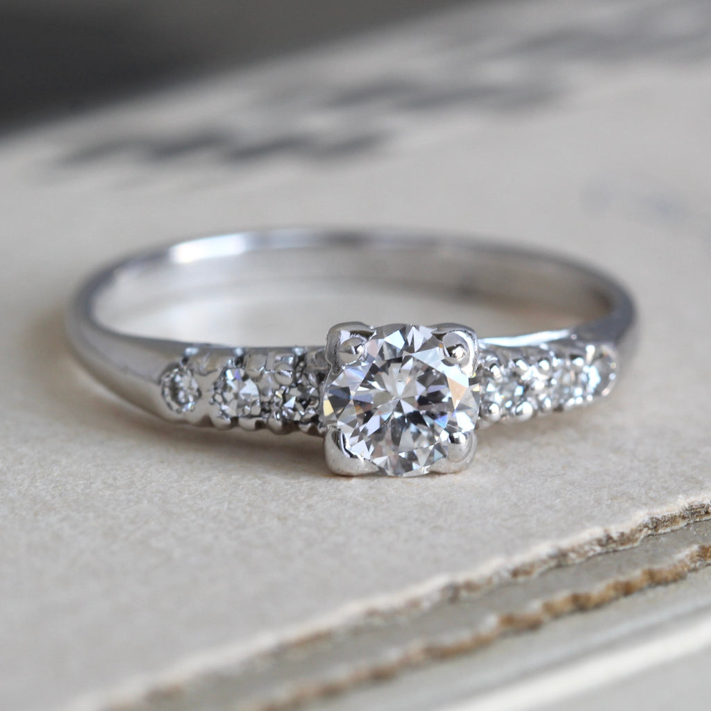   platinum engagement ring with a round diamond in the center and three smaller diamonds down each shoulder 
