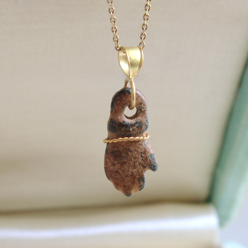 ancient bronze hand amulet charm with a gold bail and gold bracelet on a gold chain