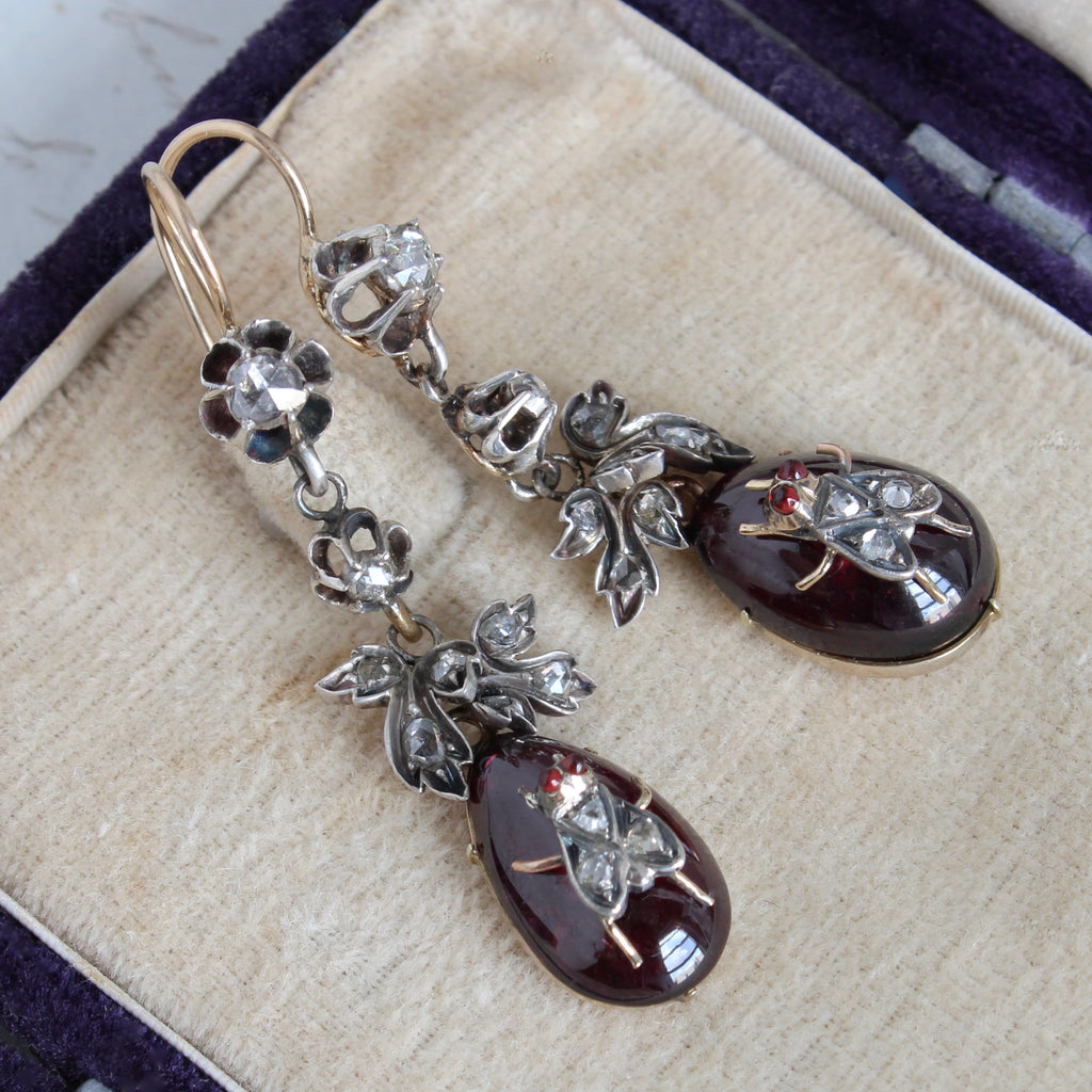 earrings with tear drop shaped garnet cabochons mounted with little silver flies that are studded with diamonds, suspended by silver diamond studded leaves in a casading style