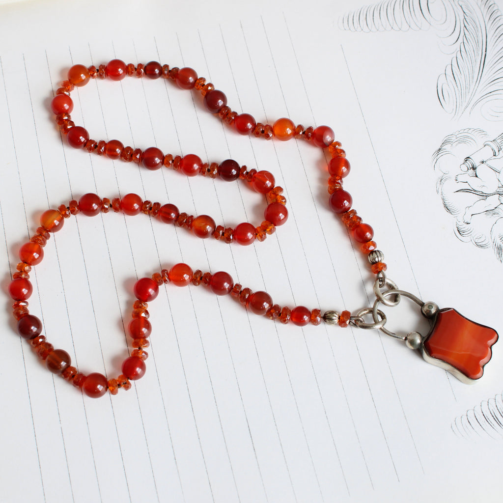 round and faceted orangey red stone beads knotted on silk with a padlock style clasp in silver