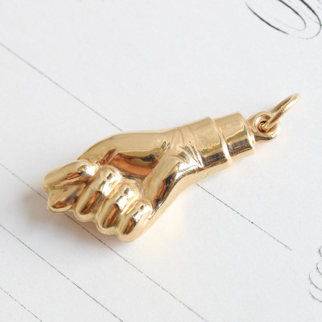 charm designed as a yellow gold hand posed in a gesture with fist clenched and thumb poking between first and second finger